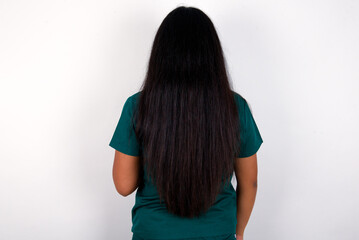 The back view of a Doctor hispanic woman wearing surgeon uniform over white wall. Studio Shoot.