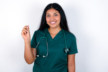 Doctor hispanic woman wearing surgeon uniform over white wall pointing up with hand showing up seven fingers gesture in Chinese sign language QÄ«.
