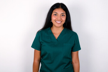 Doctor hispanic woman wearing surgeon uniform over white wall with nice beaming smile pleased...