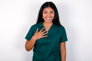 Doctor hispanic woman wearing surgeon uniform over white wall smiles toothily cannot believe eyes...
