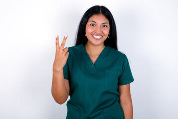 Doctor hispanic woman wearing surgeon uniform over white wall smiling and looking friendly, showing number two or second with hand forward, counting down