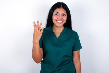 Doctor hispanic woman wearing surgeon uniform over white wall smiling and looking friendly, showing number four or fourth with hand forward, counting down