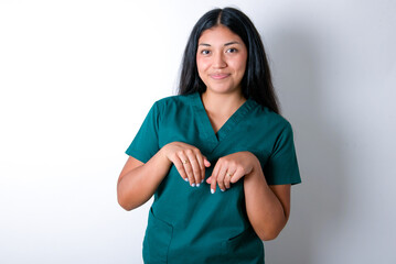 Doctor hispanic woman wearing surgeon uniform over white wall makes bunny paws and looks with innocent expression plays with her little kid