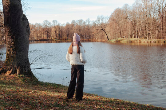 Teenage girl from behind wearing casual fall clothes in an autumn park with lake outdoors