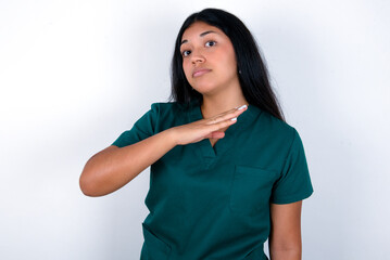 Doctor hispanic woman wearing surgeon uniform over white background cutting throat with hand as...
