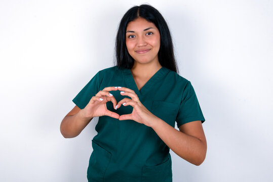 Serious Doctor hispanic woman wearing surgeon uniform over white background keeps hands crossed stands in thoughtful pose concentrated somewhere