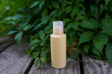 Yellow cosmetic bottle with skin care oil or lotion staying on the wood with green leaves background