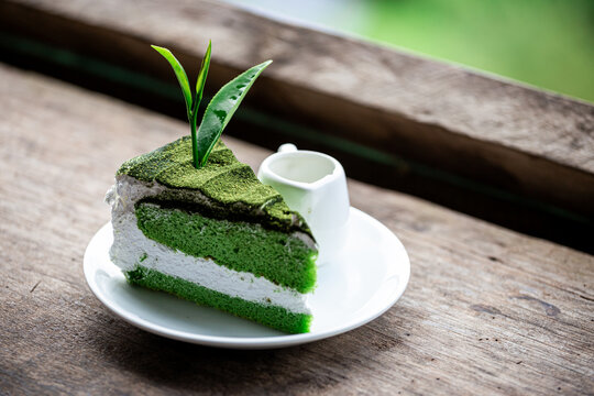 Green tea cake with matcha jam and leaf tea topping on a wooden table on plate with garden tea 