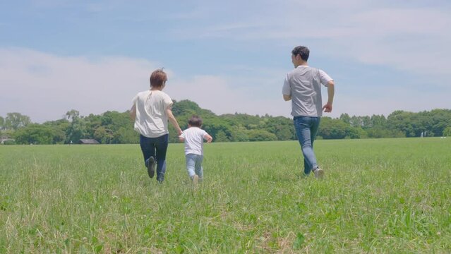 草原を走る男の子と父母の後ろ姿