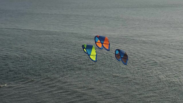 A dynamic orbital footage of three foil kites in the sky in the middle of the sea. Foil kites are soft kites based on the design of the parafoil. They can be used for a variety of different activities