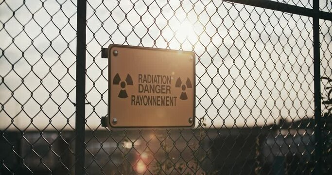 Close-up of Radiation Danger Sign Backlit by Sun on Barbed Wire Fence in Slow Motion 4K