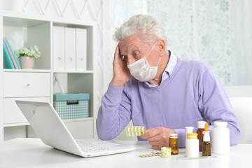 ill senior man with facial mask using laptop