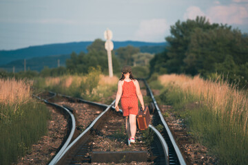 A little girl in a dress walking on an abandoned railroad tracks.