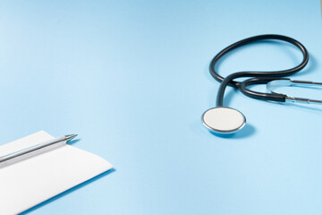 Close up view of black stethoscope and prescription pad on the blue background.