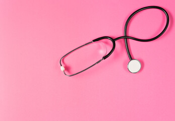 Top view of black stethoscope on the pink background.