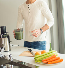 man preparing vegan fresh juice. young healthy sports guy cooks in the kitchen, cuts and whips in a...