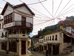 Obraz premium GJIROKASTER, ALBANIA - MARCH 28, 2022: Cobblestone street in historic center of city with traditional spring festive decorations and peculiar Ottoman era houses on background of hilltop castle tower
