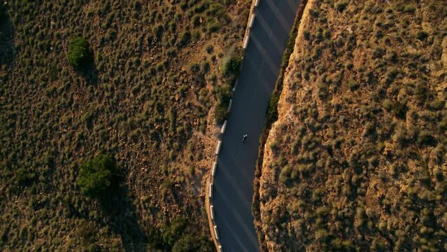 Top view drone footage of lonely cyclist ride an empty mountain road during low setting sun. Professional road cycling destination in Spain during sunset. Epic training camp for cyclists