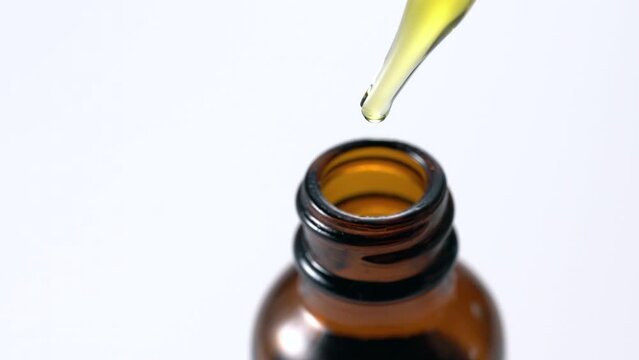Brown glass bottle on white background, cosmetic dropper drops serum. Close-up video.