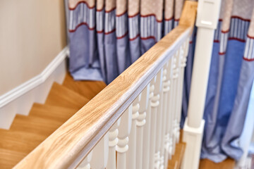 Wooden handrail of solid oak with white balusters. Classic style wooden staircase in a bright large...