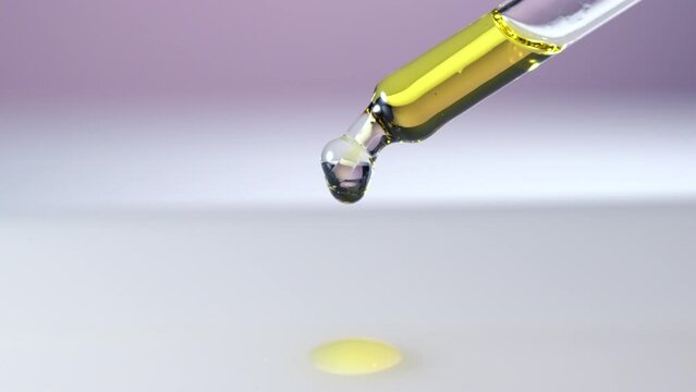 Drop of serum with glass cosmetic dropper on pink background. Close-up video.