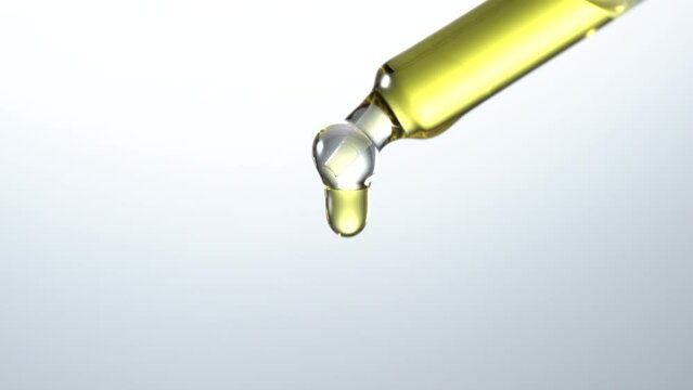 Drop of serum with glass cosmetic dropper on white background. Close-up video.
