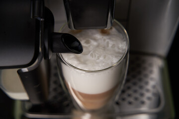 Freshly brewed latte is poured from the coffee machine into glass cups.