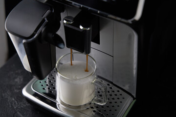 Freshly brewed cappuccino is poured from the coffee machine into glass cups.