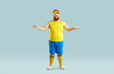 Funny happy fat young man in yellow top and blue shorts standing isolated on blue background, smiling and spreading arms in welcoming gesture inviting you to join sports gym workout for losing weight