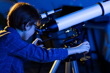 Boy carefully looks through a telescope. Smart inquisitive child explores sky through on a summer day with space maps on background. Cosmos and universe, Milky way stars. My astronomy science work © Monstar Studio