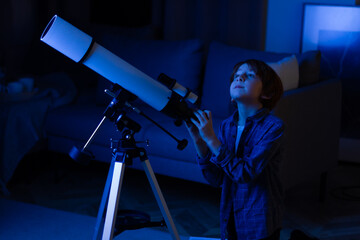 Boy carefully looks through a telescope. Smart inquisitive child explores sky through on a summer day with space maps on background. Cosmos and universe, Milky way stars. My astronomy science work