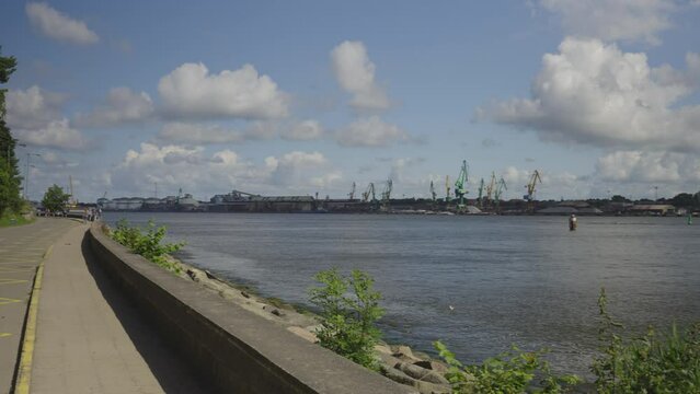 Panorama of the old port of Klaipeda from the Curonian Spit on a sunny summer day. Barges float against the backdrop of large port cranes. Tourists go to the dolphinarium along the road along the stra