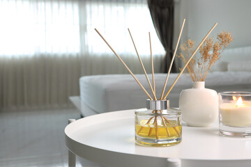 luxury aromatic scent of reed diffuser glass bottle is used as room freshener on white metal table with candle in bedroom to creat relax and romantic ambient with background of nice bed and curtain