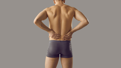 Rear view of toned muscular naked man in underwear isolated on grey studio background. Guy in...