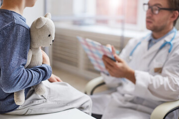 Close-up of unrecognizable little boy embracing favorite toy while answering doctors questions at...