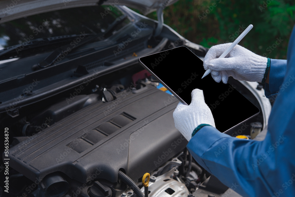 Poster close-up of man in uniform working on digital tablet while standing in front of car hood in workshop