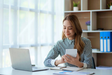 Pretty Asian business woman sitting happily working with laptop computer in the office.