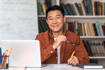 Cheerful Korean Teacher Man Near Laptop Taking Notes At Workplace