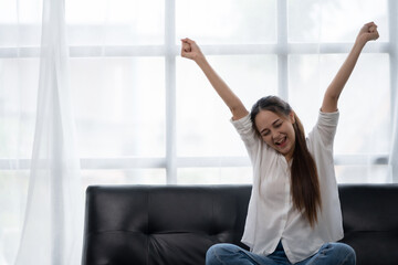 Delighted and excited Asian woman relaxing on sofa at home happily.