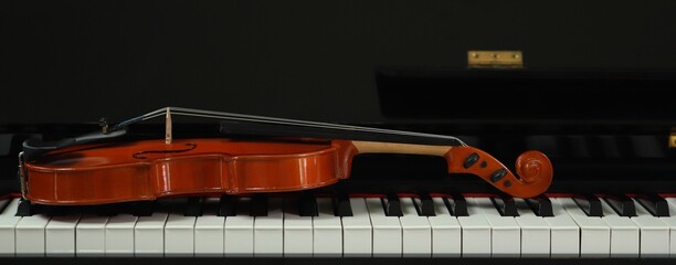 violin placed on a piano on a black background