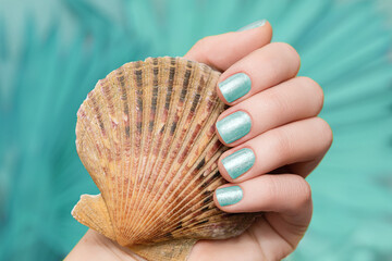 Female hand with vacation nail design. Glitter aquamarine nail polish manicure. Female hand hold...