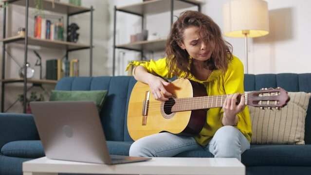 Upset caucasian woman watching guitar tutorial lesson on laptop and feeling anger with learning new tune. Concept of frustration and negative emotions.