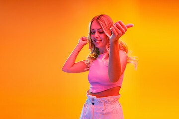 Portrait of young beautiful woman posing isolated over yellow background in neon light. Summertime party dance