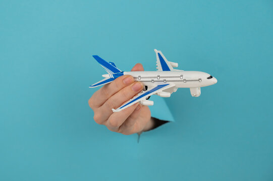A female hand sticking out of a hole from a blue background holds a model of an airplane. 