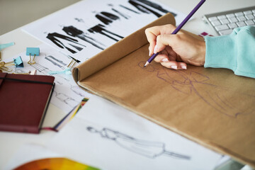 Close-up of unrecognizable fashion designer sitting at table with sketches and drawing in sketchpad