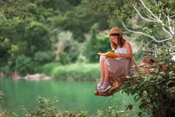Children's education. Happy little girl in a dress and a straw hat reading a book sitting on a old...