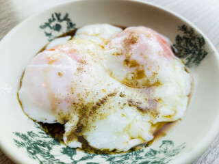 Close-up view two half boiled eggs served with soy sauce and white pepper.