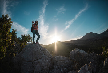 The silhouette of a woman with a backpack against the backdrop of a mountain at sunset