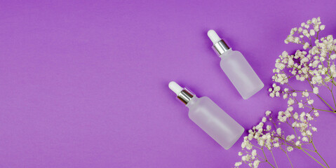 Two white bottles with skin care products on a purple background with gypsophila flowers. Skin aging problem
