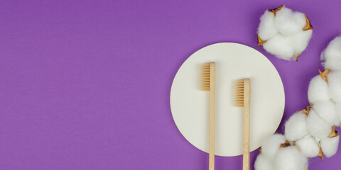 Two wooden toothbrushes and cotton flowers on a purple background. Personal hygiene items